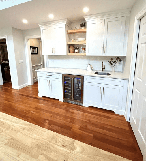 A kitchen with white cabinets and wood floors.