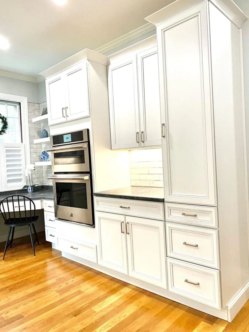 A kitchen with white cabinets and wood floors.